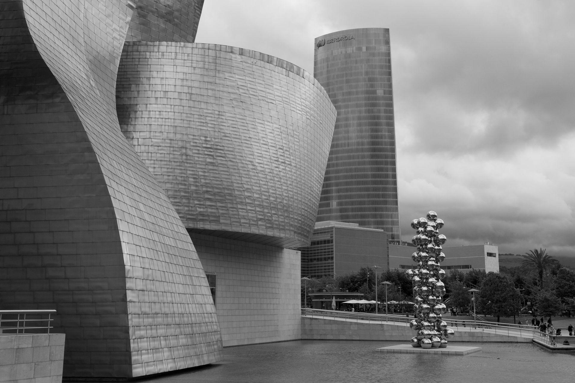 Modern architectural building with curved, metallic surfaces and adjacent sculpture made of reflective spheres.